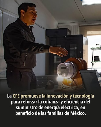 Hombre en chaqueta negra gesticulando, de pie junto a un medidor de electricidad digital montado en una base de madera con una bombilla encendida