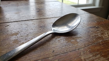 Una cuchara de metal brillante sobre una mesa de madera rústica, con una ventana parcialmente visible en el fondo.