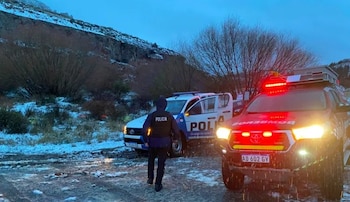 Un agente de policía, un vehículo policial blanco y azul, y un vehículo de bomberos rojo con luces encendidas en un camino con nieve