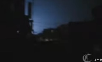 Imagen oscura y borrosa de una calle de noche con cielo azul oscuro. Se observan luces difusas en la distancia y un logo con la letra C en la esquina inferior derecha
