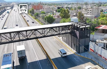 Vista aérea de una autopista con vehículos, un puente peatonal techado y una estructura de estación con estructura metálica y vidrio