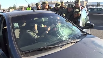 Agentes con uniforme verde rodean un auto con el parabrisas roto mientras una persona en el interior mira hacia ellos
