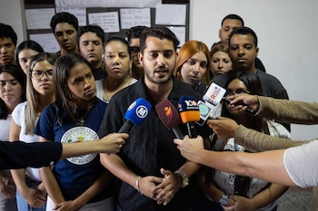Un hombre con barba habla a micrófonos de prensa, rodeado por varios jóvenes. Una mujer viste una camiseta de la Universidad Central de Venezuela