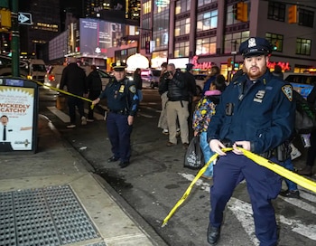 Dos policías uniformados en la calle por la noche, uno sosteniendo cinta amarilla de escena del crimen, con edificios iluminados y gente al fondo en Times Square