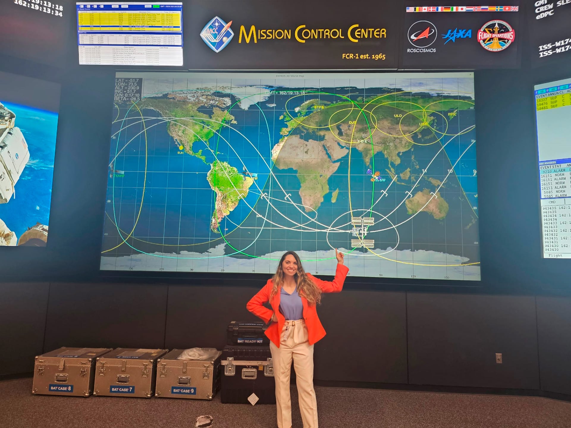 Lorna Evans de la NASA posa frente a una pantalla gigante que muestra un mapa mundial con órbitas satelitales en el Centro de Control de Misión.