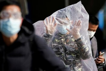 A passenger wearing a mask and covered with a plastic bag walks outside the Shanghai railway station in Shanghai, China, as the country is hit by an outbreak of a new coronavirus, February 9, 2020. REUTERS/Aly Song TPX IMAGES OF THE DAY