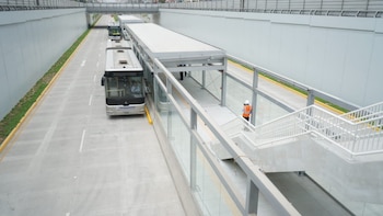 Un autobús de transporte público permanece junto a una estación techada con escaleras dentro de una vía de concreto