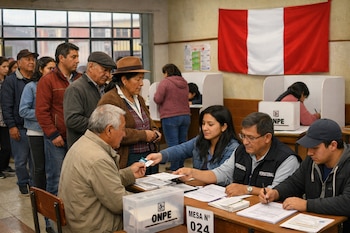Peruanos en fila en un centro de votación. Miembros de mesa revisan identificaciones y entregan cédulas, con cabinas de votación y la bandera de Perú visible.