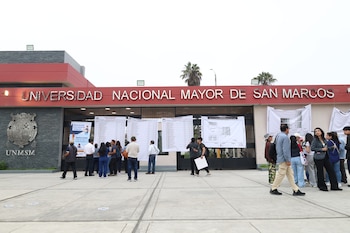 Entrada principal de la Universidad Nacional Mayor de San Marcos con su letrero y escudo. Varias personas consultan listas y mapas de votación en carteles