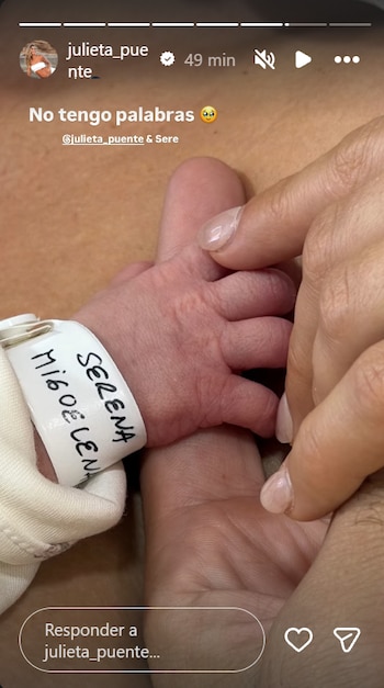 Mano de un adulto sosteniendo la mano de un bebé con una pulsera de identificación. La pulsera dice 'SERENA Migoel Lena'
