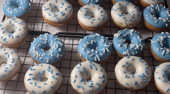 Dieciséis donas glaseadas en azul y blanco con grageas sobre una rejilla metálica.