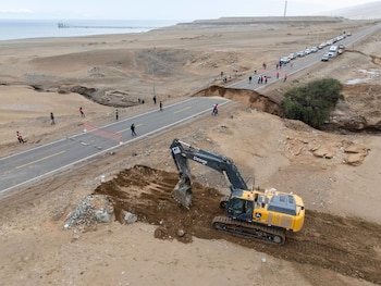 Una excavadora trabaja en una carretera interrumpida en medio de un paisaje desértico, mientras personas y vehículos esperan en un lateral