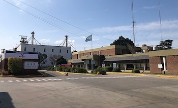 Entrada a una planta industrial con un cartel de Molinos, un mástil con la bandera argentina, edificios de ladrillo y silos al fondo