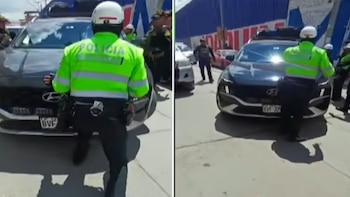 Un agente de policía con chaleco reflectante verde y casco blanco se coloca frente a un automóvil oscuro en una calle