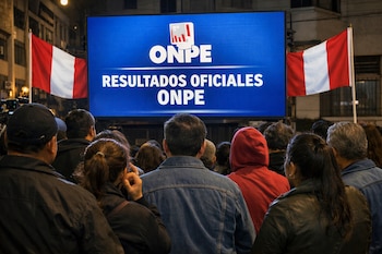 Vista trasera de una multitud de personas de pie observando una gran pantalla azul que muestra "ONPE RESULTADOS OFICIALES ONPE", flanqueada por dos banderas de Perú.