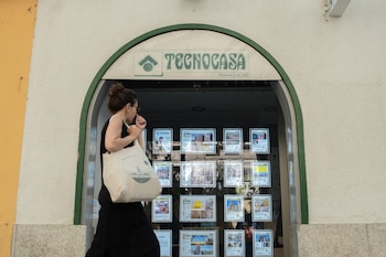 Una mujer mira los anuncios de viviendas en alquiler y compra que tiene en su escaparate una inmobiliaria.