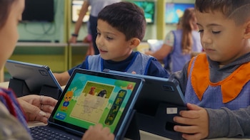 Dos niños sentados en una mesa manipulan pantallas táctiles de tabletas digitales con juegos interactivos