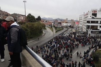 Primer plano de un oficial de la Policía Boliviana con equipo antidisturbios asistiendo a una mujer mayor de cabello gris; otros agentes en línea detrás