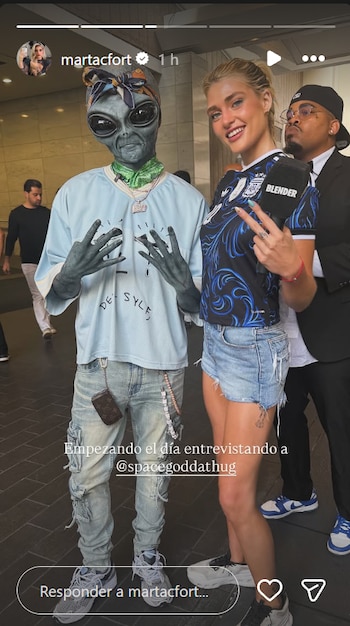 Marta Fort con camiseta de Argentina, micrófono, posa junto a persona disfrazada de alienígena con pañuelo y un hombre con traje