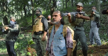 Grupo de seis hombres en un bosque. Varios usan indumentaria táctica, chalecos y sostienen armas de airsoft. Un hombre con barba viste camisa y chaleco de jean
