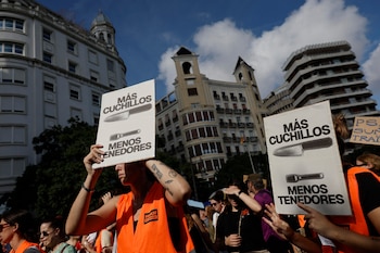 Varias personas con chalecos naranjas sostienen carteles con la imagen de un cuchillo y un tenedor frente a edificios antiguos