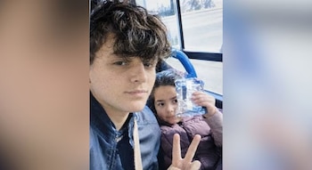 Un joven se toma un autorretrato junto a una niña que sostiene un envoltorio y hace el signo de la paz dentro de un autobús