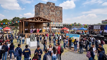 Estudiantes caminan junto a un escenario de danza, una zona de pintura colectiva y la Biblioteca Central al fondo.
