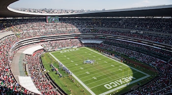 Vista aérea de un estadio lleno de personas donde se disputan jugadas sobre un campo de fútbol americano marcado con yardas.