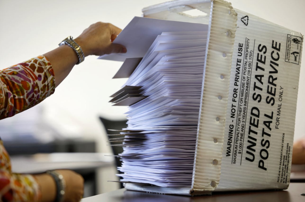 Una mano coloca sobres de boletas de voto por correo en una caja del Servicio Postal de Estados Unidos durante el proceso de elecciones primarias. (Jonathan Drake/REUTERS)