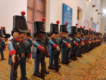 Una fila de figuras de juguete de plástico vestidas con uniformes azules y sombreros negros que sostienen fusiles sobre una superficie de tierra