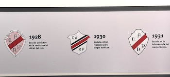 Una vitrina en el Museo River mostrando tres escudos históricos de River Plate con sus respectivos años y descripciones en español