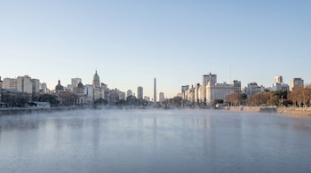 Vista panorámica del Río de la Plata con neblina baja y la silueta de edificios de Buenos Aires al fondo, incluyendo el Obelisco y cúpulas de edificaciones.