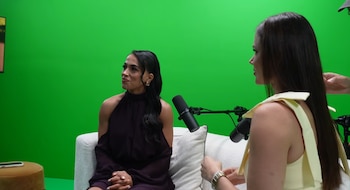 Dos mujeres sentadas frente a micrófonos en un estudio con pantalla verde. Una mujer mira hacia la izquierda, la otra, de perfil, hacia la derecha