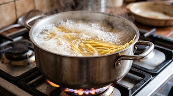 Olla de metal con agua hirviendo y espaguetis sobre la llama encendida de una cocina de gas.