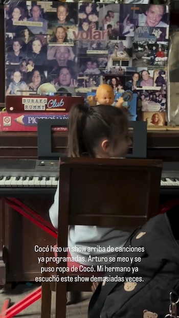 Una niña frente a un teclado electrónico; detrás, un mural de fotos familiares y juegos de mesa, incluyendo un muñeco bebé sobre el teclado