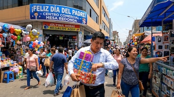 Un hombre con tres regalos envueltos y bolsas mira su reloj en una calle concurrida; una mujer sonriente señala, y un cartel dice "¡Feliz Día del Padre!".