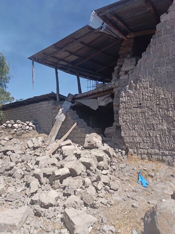 Pared de adobe colapsada con escombros acumulados en el suelo debajo de un techo de chapa ondulada sostenido por vigas de madera