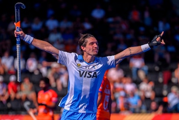 Un jugador de hockey con camiseta celeste y blanca celebra con los brazos extendidos y lleva un palo en la mano