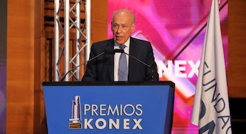 Un hombre de traje habla ante dos micrófonos en un atril azul con las palabras Premios Konex, junto a una bandera institucional blanca