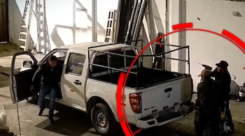 Una camioneta blanca con estructura metálica en un estacionamiento interior, con tres personas alrededor y escaleras contra la pared.