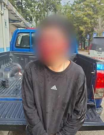 Dos agentes de policía con uniforme azul conducen a un hombre con polo naranja y rostro borroso