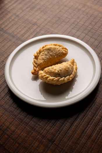 Dos empanadas fritas de color dorado, una completa y otra ligeramente cortada, servidas en un plato blanco redondo sobre una superficie de madera oscura y texturizada