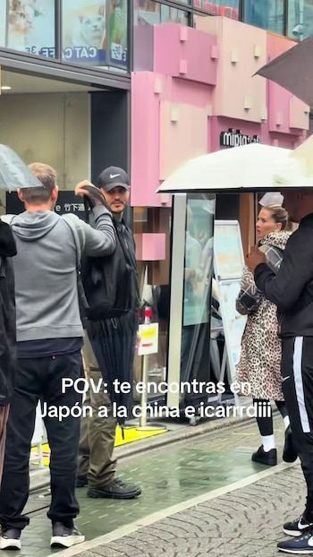 Mauro Icardi y La China Suárez caminan por una calle de Japón bajo la lluvia. Icardi lleva gorra negra y paraguas; Suárez, un abrigo estampado. Hay edificios rosas y carteles en japonés al fondo