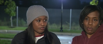 Dos mujeres al aire libre de noche, una con gorro gris y chaqueta oscura y otra con sudadera granate