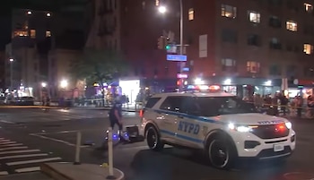 Un patrullero con luces de emergencia y cinta policial acordonan un cruce nocturno en la calle mientras un agente examina la escena