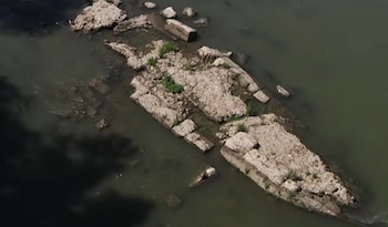 Vista aérea de un río con grandes formaciones rocosas de color claro, parte de ellas expuestas con vegetación y otras sumergidas. Sombra oscura a la izquierda