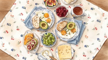 Vista superior en acuarela de una mesa con platos de huevos, aguacate, pan, frambuesas, uvas, higos, queso y una taza de café.
