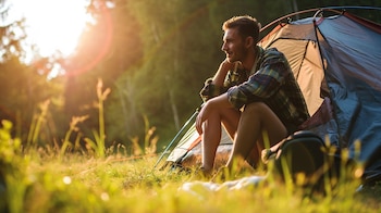 Un aventurero preparando su carpa en una zona de camping rodeada de montañas nevadas, cerca de un lago y un río. La imagen captura el espíritu del turismo de aventura y las vacaciones en entornos naturales, donde la preparación para el frío es esencial. Ilustra la conexión entre el ser humano y la naturaleza, y la búsqueda de experiencias únicas lejos del bullicio urbano. (Imagen ilustrativa Infobae)