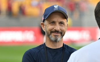 Plano medio de un hombre con barba y gorra azul con el escudo del Liverpool FC que sonríe en un estadio