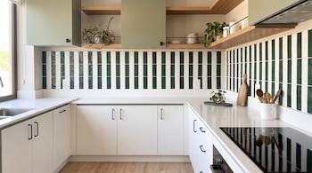 Cocina con muebles blancos, mesadas blancas, estantes de madera, gabinetes superiores verdes, revestimiento de pared a rayas verdes y blancas, fregadero, cocina, horno, plantas.